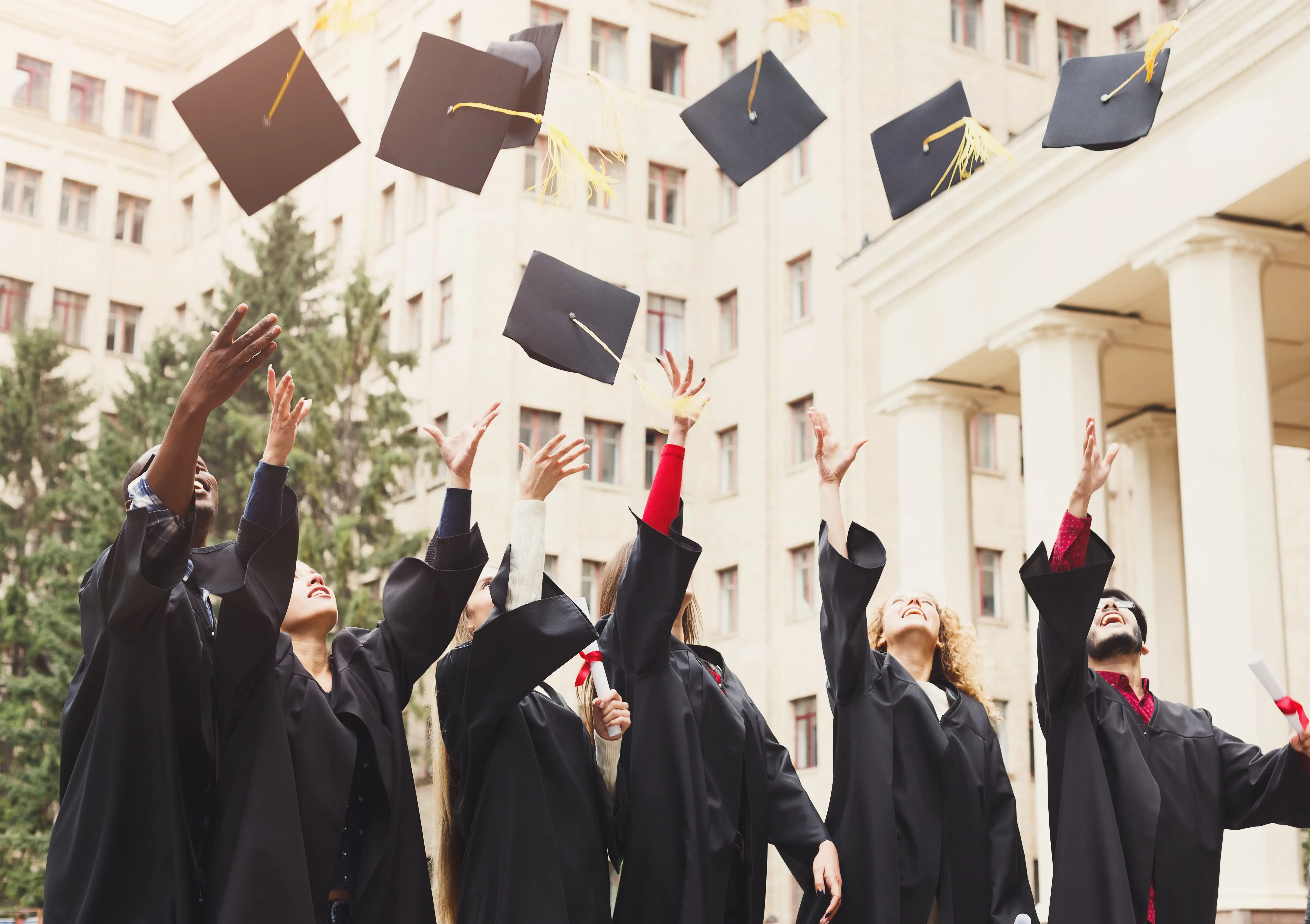 A group of people in black graduation gowns throwing their graduation caps
