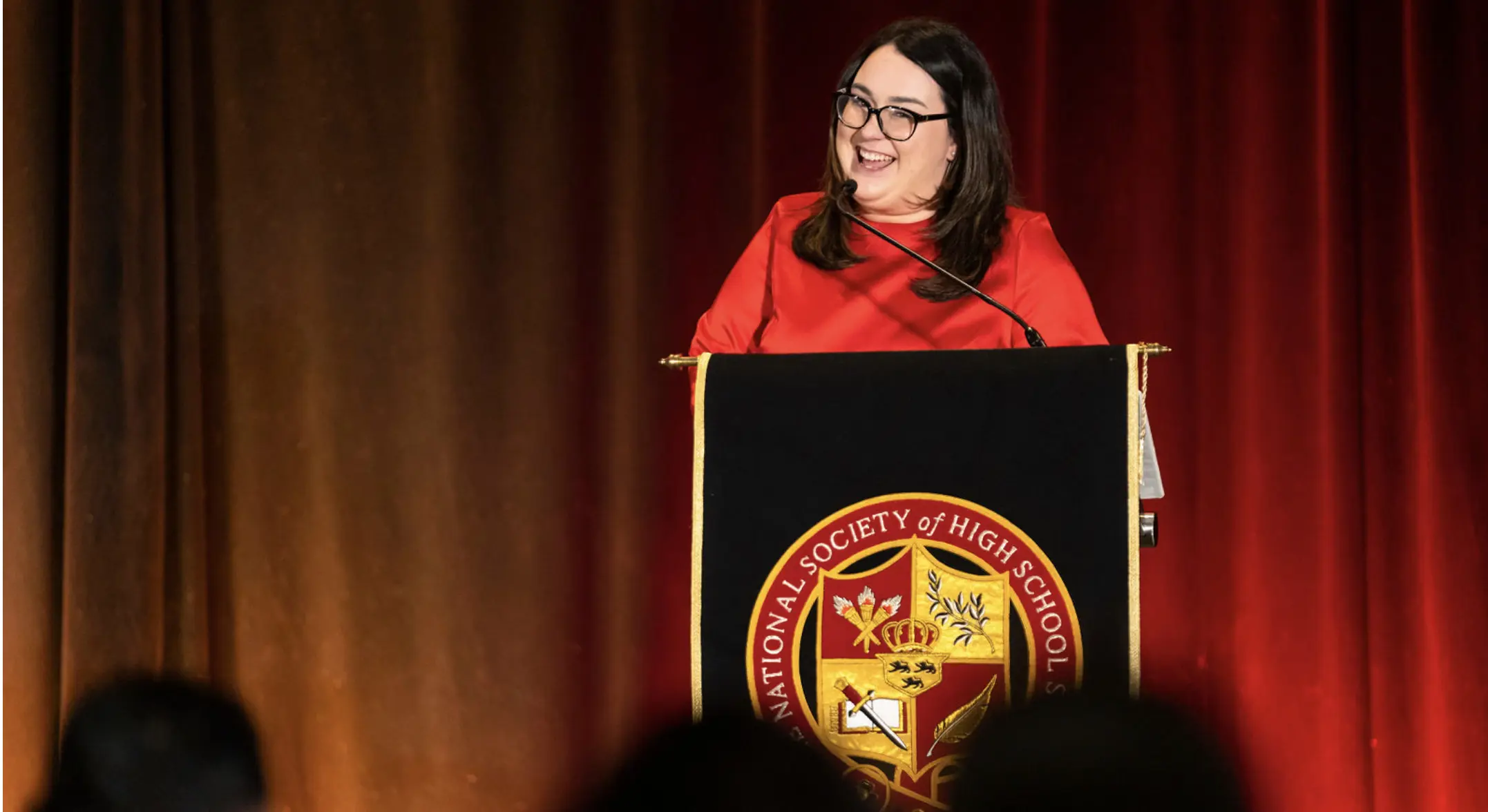 Woman speaking at podium with NSHSS Emblem